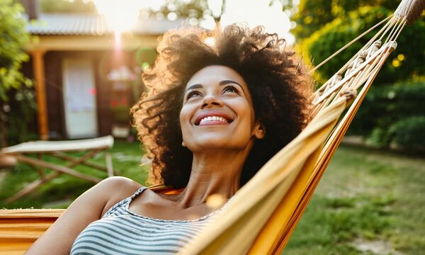 A joyful woman unwinds in a hammock, basking in the golden sunlight of a tranquil garden setting