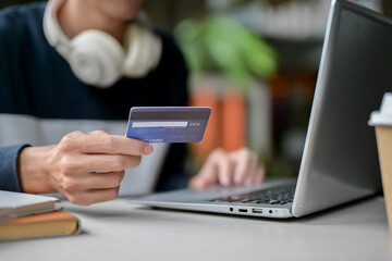 A close-up image of a man holding a credit card over a table while using his laptop.