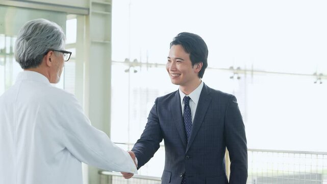 白衣の技術者と握手するビジネスマン