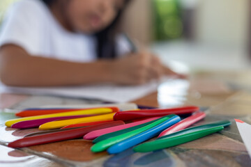 A child is drawing with crayons on a table. The crayons are in a rainbow of colors and are scattered across the table.