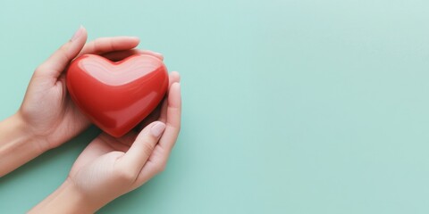 Obraz premium A person holds a vibrant red heart, symbolizing love and care, against a soft mint background.