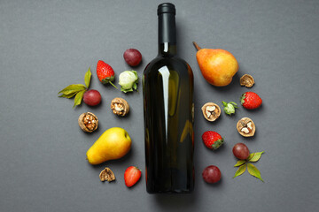 A bottle of wine with flowers and fruits, on a gray background.