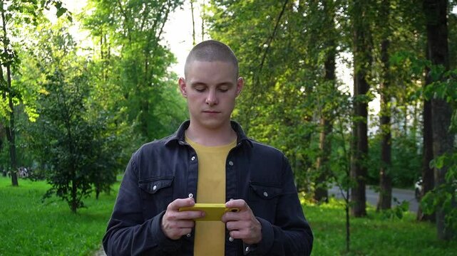 teenager is playing on a mobile phone while standing in the park. mobile game tester.