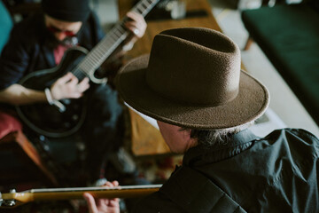Rear view closeup of unrecognizable musician wearing hat sitting in front of his friend playing guitars