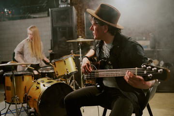 Fototapeta premium Medium shot of mature Caucasian man playing electric bass guitar in modern rock band, copy space