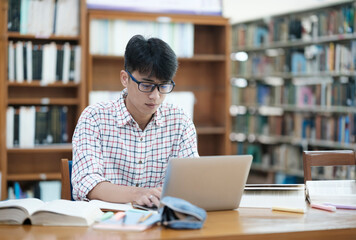 Young Asian male sitting inside a library alone doing research. Man working on a project. Young man doing research for a case.