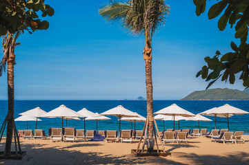 beach umbrellas with sun beds without people on the sandy beach of Nha Trang against the background of the sea or ocean and palm trees