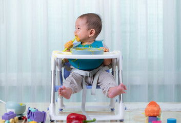 A little child eating his first meal on a high chair for children