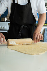 Hands of a man baking dough with rolling pin on white table