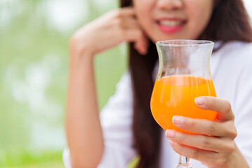 Women hands drink orange juice fresh fruit cool drinking in green park garden. Asian women hands holding healthy drinking glass. Beautiful female pouring orange juice from cocktail bottle outdoors