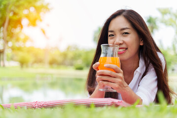 Asian Women picnic in green park smilng face hands holding glass of orange juice fresh fruit cool...
