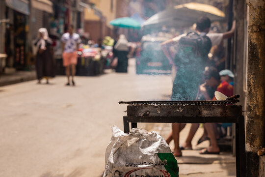 Coal grill being fired up on the market streets of Oran, Algeria. side view of a commercial grill at a market in arab country. Bag of coal next to it, people behind