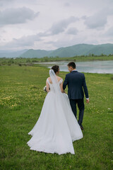 A bride and groom are walking together in a field. The bride is wearing a white dress and the groom is wearing a blue suit. The scene is peaceful and serene