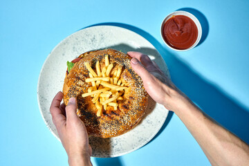 burger served on sesame bagel. The burger is topped with of crispy French fries, creating a unique and eye-catching presentation.