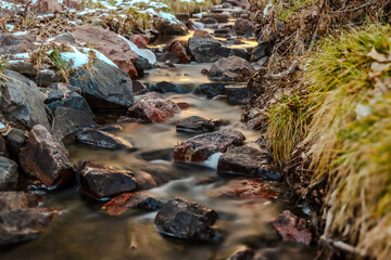Stream flowing through partially snowy rocks in a forest