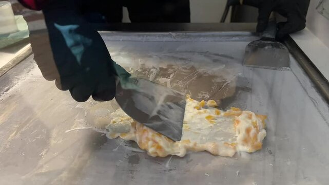 Thai roll ice cream is made by hand in black gloves on the freezer. Sweet dessert made from natural berries and ingredients. The process of making food. The art of cooking Thai ice cream on the street
