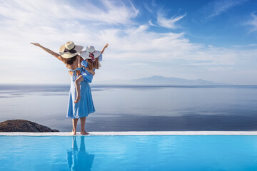 A happy mother and her daughter are standing by the pool and enjoying the summer sunset over the mediterranean sea