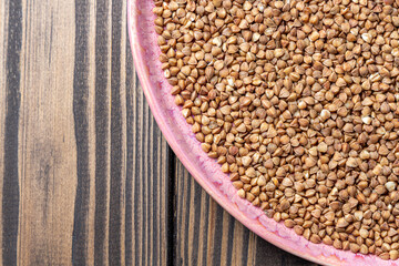 Buckwheat Grains on Plate on Wooden Background, Top View, Copy Space.Hulled kernels of buckwheat grains close up. Food background.