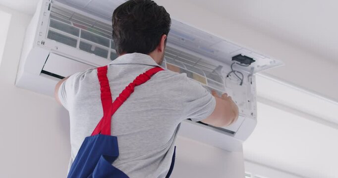 Electrician man maintaining modern air conditioner standing on a ladder indoors. Young male technician repairing and changing filter in air conditioner in new apartments. 4k video.