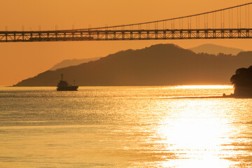 瀬戸大橋を渡る列車と夕陽が映える瀬戸内海を遠望する