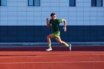 Obraz premium Young athlete man in uniform, sprinter running in motion on track to finish line. Speed and victory. Dynamic and energy. Concept of sport, tournament, motivation, workout, competition. Ad
