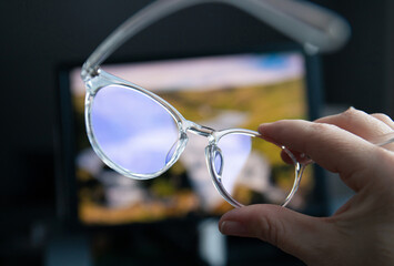 Selective focus on transparent clear blue light computer glasses and computer screen glowing on the background in home or office. Blue light glasses protect eyes and eyesight from screens blue light.