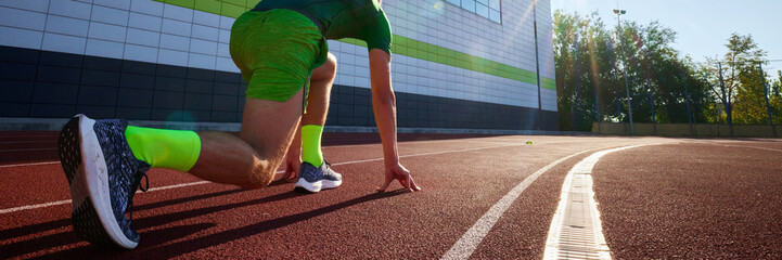 Banner. Rear view of young man, athlete in low start position, ready to running fast to finish line. Sportsman ready to get win. Concept of sport, tournament, motivation, workout, competition. Ad