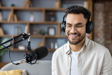 Smiling man in headphones recording podcast in studio with microphone, enjoying conversation and audio production