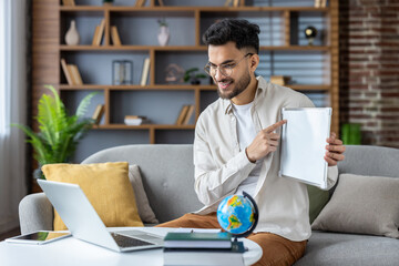 Smiling man pointing at blank whiteboard during online lesson with laptop on couch at home office setting