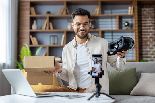 Young man creating unboxing video content with virtual reality headset and smartphone in modern home studio - Powered by Adobe