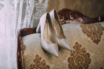 A pair of silver high heels are on a couch. The couch is brown and has a floral pattern