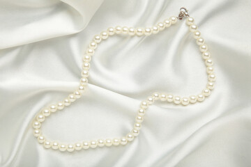 Pearl necklace on white silk background. Top view