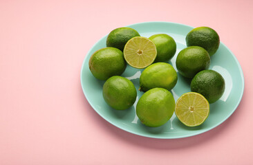Green lime with cut in half on plate on pink background.