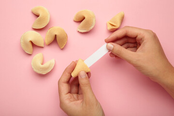 Woman holding tasty fortune cookie and paper with prediction on pink background. Space for text
