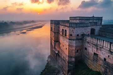 Fototapeta premium An ancient fortress overlooks a tranquil river while shrouded in gentle mist, bathed in the warm hues of sunset, showcasing the harmonious blend of nature and history.