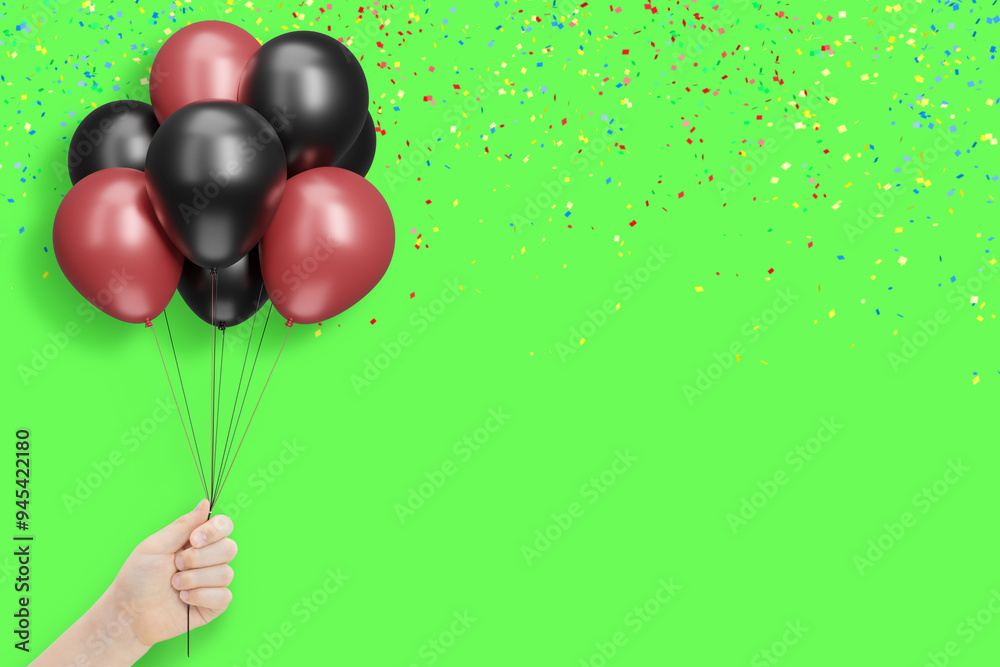 Poster female hand holds bunch of red and black balloons on green background with confetti. empty space for