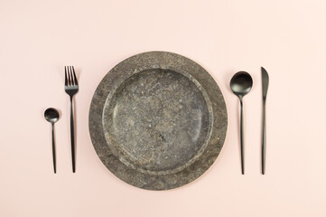 Top view of brown marble tray and plate, black cutlery on pink background. Food presentation, stone...