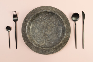 Top view of brown marble tray and plate, black cutlery on pink background. Food presentation, stone...