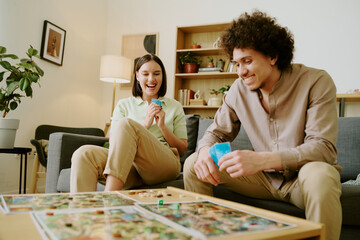 Joyful young biracial couple having fun playing modern fantasy board game in living room at home