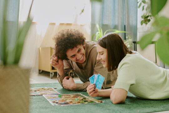 Happy young biracial couple playing modern board game while relaxing on floor in cozy living room at home - Powered by Adobe