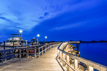 Illuminated wooden walkway by the sea after sunset at blue hour