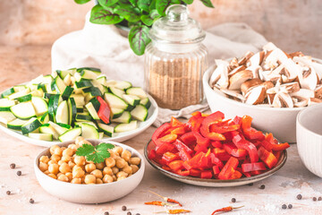 Chickpeas, sliced zucchini, red peppers and mushrooms in bowls in preparation for cooking