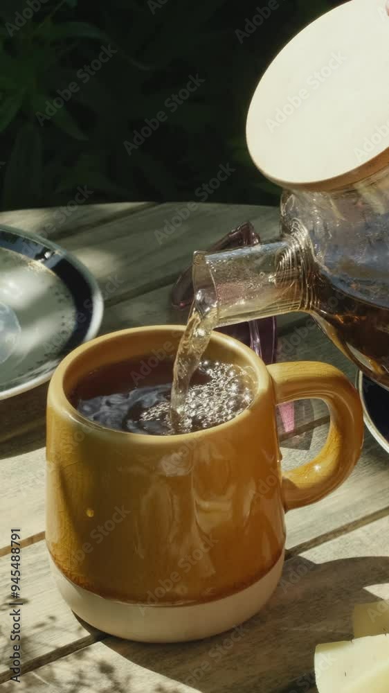 Poster Vertical video. Woman pouring tea into ceramic mug on wooden garden table.