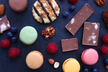 Macarons, chocolate, cookies, berries and various nuts on dark blue background. Top view.