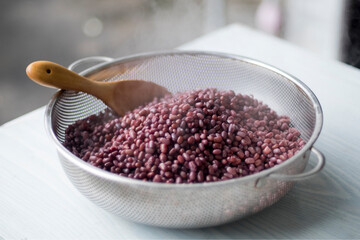 Cooked Azuki bean (Adzuki bean or red kidney bean) with wooden ladle in stainless steel sieve for reduce temperature closed up selective focus and blur background. Prepared to making tempeh or tempe.