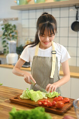 Pretty young asian woman wearing an apron preparing a fresh salad in modern kitchen