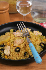 Assiette de semoule estivale avec des morceaux de poulet, des olives noires, du maïs et une rondelle de citron confit