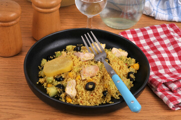 Assiette de semoule estivale avec des morceaux de poulet, des olives noires, du maïs et une rondelle de citron confit