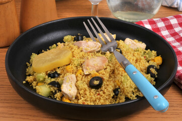 Assiette de semoule estivale avec des morceaux de poulet, des olives noires, du maïs et une rondelle de citron confit