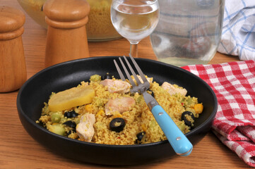 Assiette de semoule estivale avec des morceaux de poulet, des olives noires, du maïs et une rondelle de citron confit